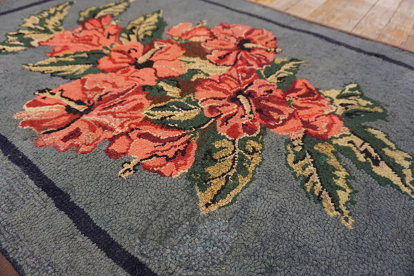 Nubby blue-gray rug featuring large coral and green floral motifs, shown close-up on a wood floor.