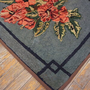 Low-pile rug in dusty blue with coral floral motifs and a dark geometric border over rustic wood.