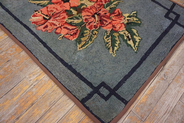 Low-pile rug in dusty blue with coral floral motifs and a dark geometric border over rustic wood.