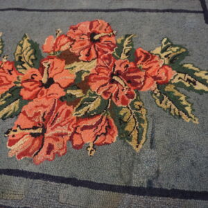 Textured rug displays coral-red flowers and olive green leaves on a blue field with a dark Greek key border.