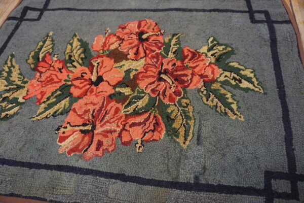 Textured rug displays coral-red flowers and olive green leaves on a blue field with a dark greek key border.