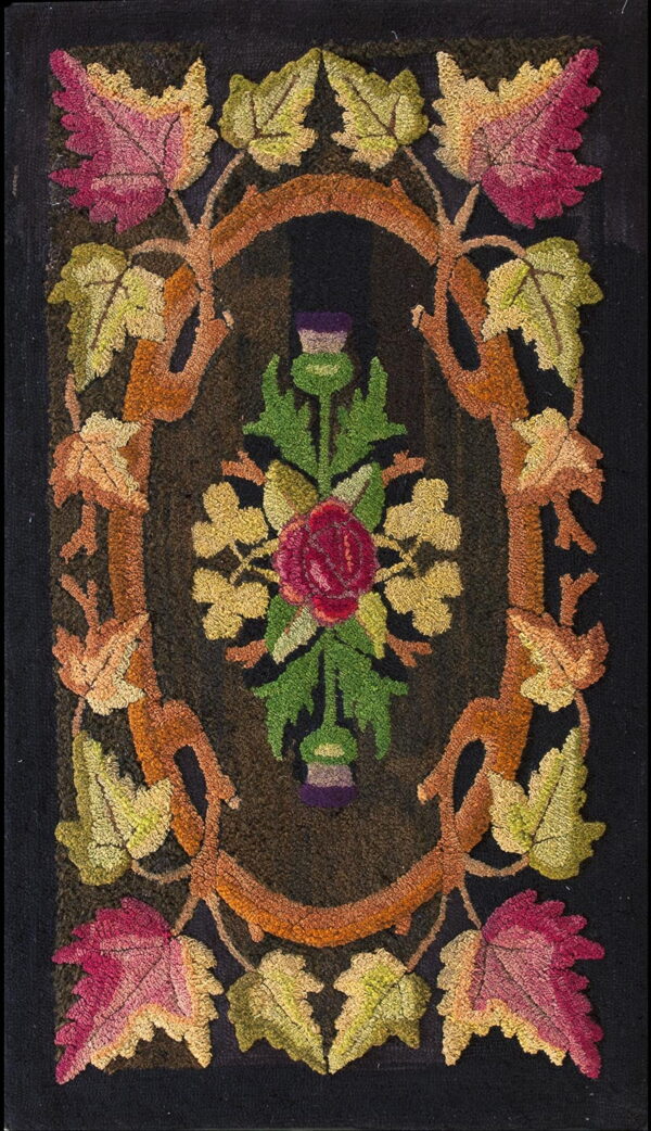 A dark hooked rug features a vine oval border framing a central red rose and colorful autumn leaves.