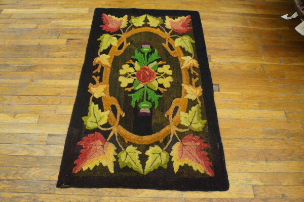 Dark hooked rug featuring a colorful floral medallion and autumn leaves on a light plank wooden floor.