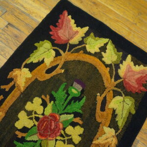 Hooked black rug featuring brightly colored autumn leaves, vines, and flowers on wood flooring.