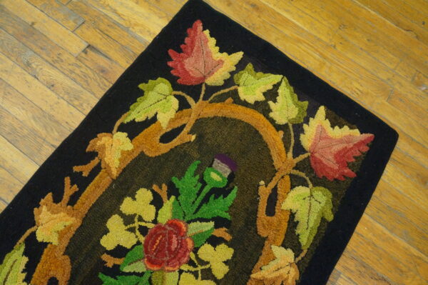 Hooked black rug featuring brightly colored autumn leaves, vines, and flowers on wood flooring.