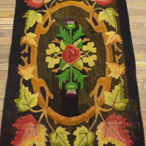 Dark hooked rug with an autumn-colored floral and vine design on light brown hardwood flooring.