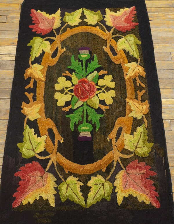 Dark hooked rug with an autumn-colored floral and vine design on light brown hardwood flooring.