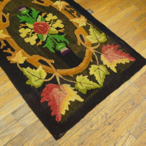 Black hooked rug with a central red, yellow, and green floral vine design on distressed wooden planks.