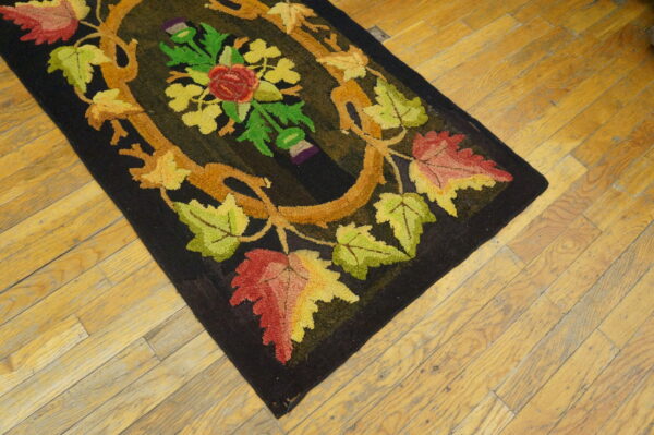 Black hooked rug with a central red, yellow, and green floral vine design on distressed wooden planks.
