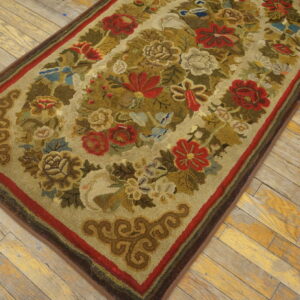Rustic hooked rug with red, green, and tan floral patterns on distressed wood flooring.