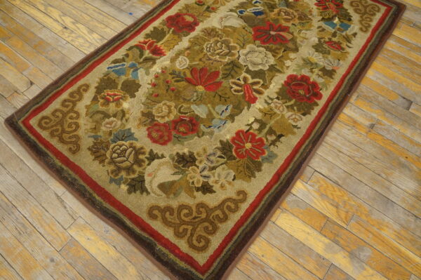 Rustic hooked rug with red, green, and tan floral patterns on distressed wood flooring.