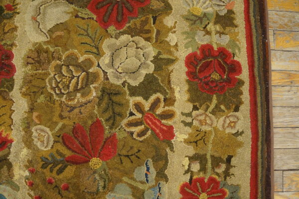 Close-up of a hooked floral rug displaying muted reds, creams, and olive greens on wooden floors.