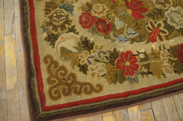 Textured tan rug with dense red, green, and brown floral patterns borders rustic wood flooring.