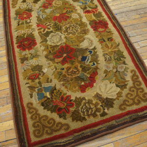 Floral hooked rug in muted red, green, and gold colors lying on rustic wood plank flooring.