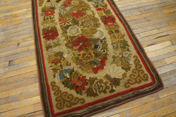 Floral hooked rug in muted red, green, and gold colors lying on rustic wood plank flooring.