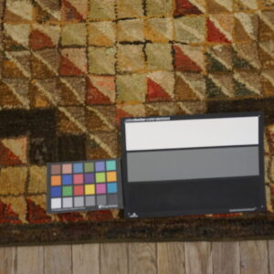 Textured rug with a brown, red, and green checkerboard pattern and color calibration charts on wood floor.