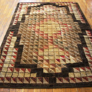 Textured geometric rug in shades of tan, brown, and red on a distressed hardwood floor.