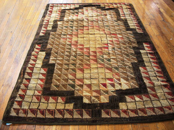 Textured geometric rug in shades of tan, brown, and red on a distressed hardwood floor.