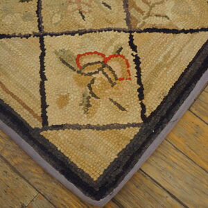 Textured beige rug with dark grid pattern and red floral accents rests on light brown plank flooring.