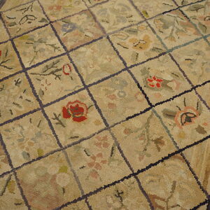 A beige rug features a segmented diamond grid with dense floral motifs in muted reds and greens on wood flooring.