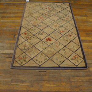Beige diamond lattice rug with colorful floral motifs rests on worn orange-toned wood flooring.