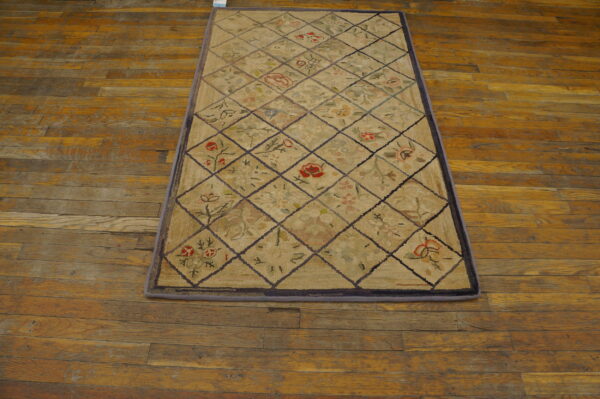 Beige diamond lattice rug with colorful floral motifs rests on worn orange-toned wood flooring.