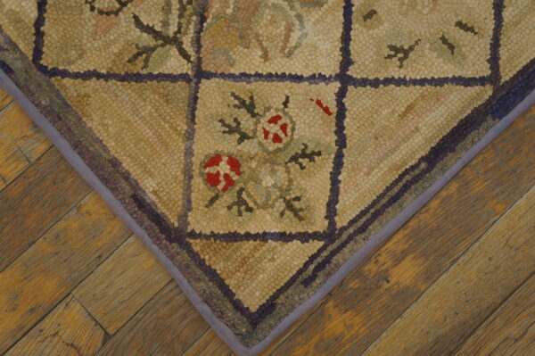 Textured corner of a beige and purple grid rug with red floral accents lying on rustic wood flooring.