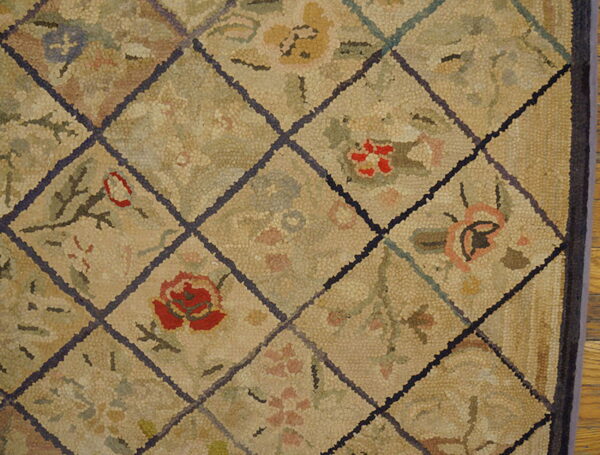 Muted beige rug with a textured surface, featuring red and pink floral motifs inside a dark diamond grid.