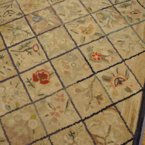 Textured beige rug featuring a dark grid and colorful floral designs lying on plank hardwood flooring.