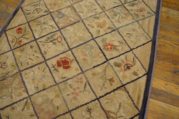 Textured beige rug featuring a dark grid and colorful floral designs lying on plank hardwood flooring.
