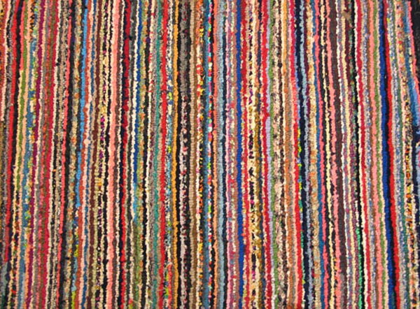 Close-up of a multicolored rug with tightly packed vertical striped rows and an uneven texture.