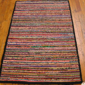 A brightly colored, textured rug featuring narrow horizontal stripes rests on a warm plank wood floor.