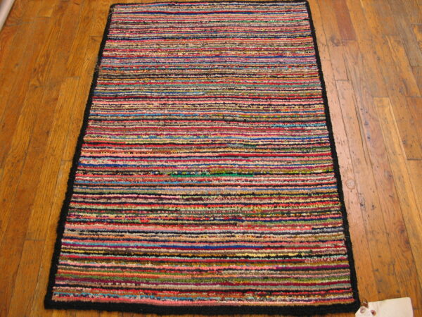 A brightly colored, textured rug featuring narrow horizontal stripes rests on a warm plank wood floor.