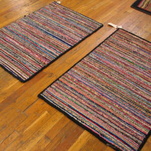 Two colorful, striped rag rugs with black borders lie diagonally on a worn wooden floor.