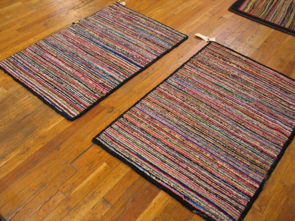 Two colorful, striped rag rugs with black borders lie diagonally on a worn wooden floor.