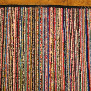 Multicolored striped rag rug with a black border lying on natural wood plank flooring.