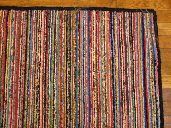 Multicolored striped rag rug with a black border lying on natural wood plank flooring.