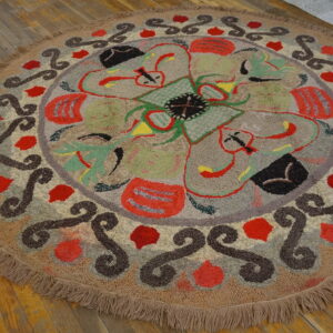 Round, looped beige rug with colorful abstract florals and dark scrollwork on wood planks.