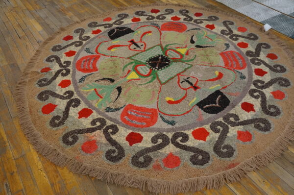 Round, looped beige rug with colorful abstract florals and dark scrollwork on wood planks.