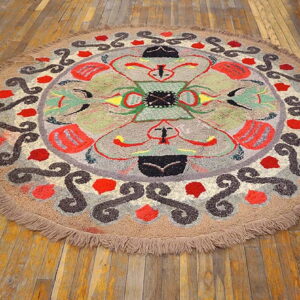 Textured round rug with an abstract multicolored pattern and thick fringe resting on worn wooden planks.