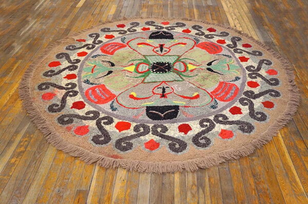 Textured round rug with an abstract multicolored pattern and thick fringe resting on worn wooden planks.
