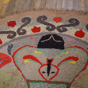 High-pile multicolor hooked rug with abstract shapes and swirls rests on distressed wooden floorboards.