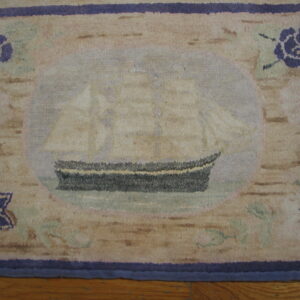 Beige and purple low-pile rug with a sailing ship medallion rests on a wood plank floor.
