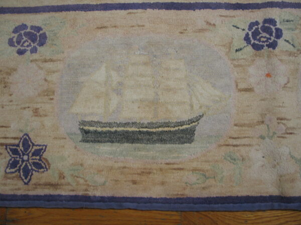Beige and purple low-pile rug with a sailing ship medallion rests on a wood plank floor.