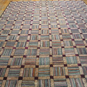 Large grid rug with tan borders and multi-colored striped blocks, connected by purple squares on a wood floor.