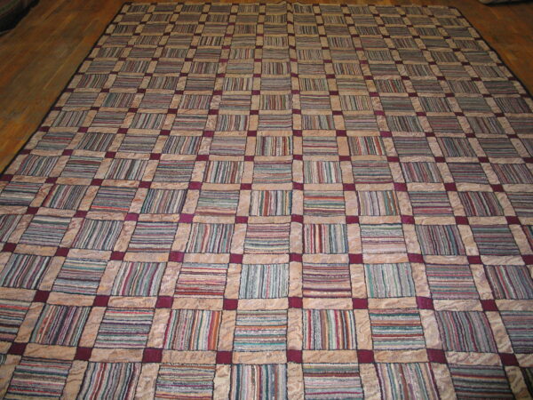 Large patchwork rug featuring a beige and maroon grid filled with multicolor striped squares on a wood floor.
