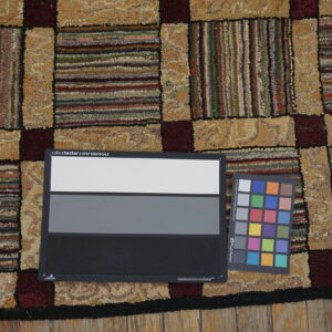 Patchwork rug with nubby texture displays tan, maroon, and multi-colored striped blocks on wood flooring.