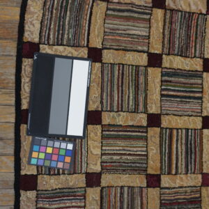Multicolored checkered rug featuring textured beige and striped blocks separated by burgundy lines on wood planks.
