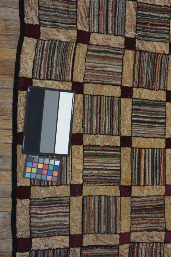 Multicolored checkered rug featuring textured beige and striped blocks separated by burgundy lines on wood planks.