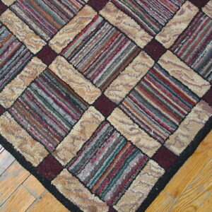 A textured diagonal patterned rug with multicolored striped blocks and looped beige borders on wood flooring.